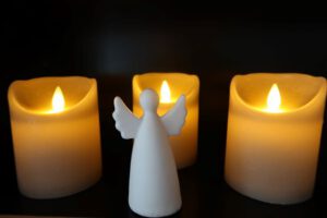 Ein weißer Porzellanengel steht vor drei dicken Kerzen
